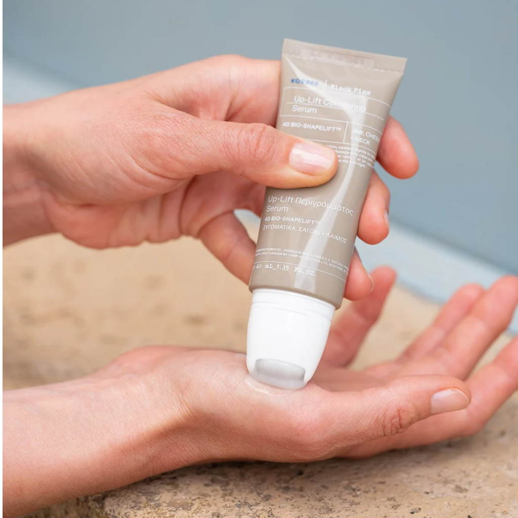 Hands dispensing KORRES Black Pine Up-Lift serum using ON/OFF roller head