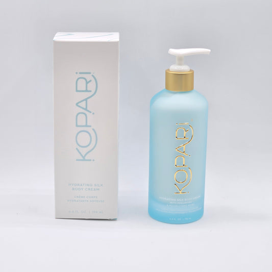 Kopari Hydrating Silk Body Cream: 6.6 fl oz light blue pump bottle with gold accents, beside its white box.