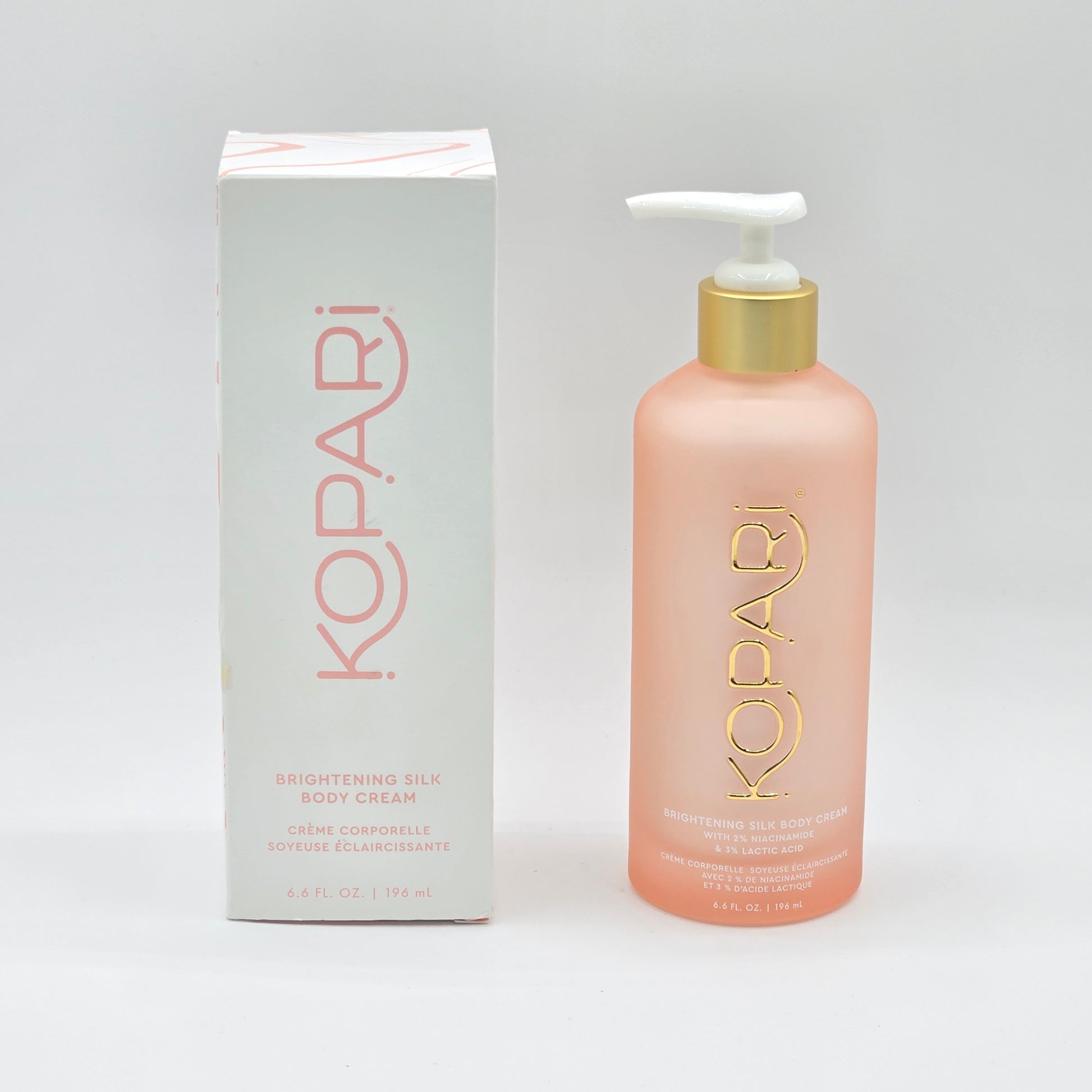 Kopari Brightening Silk Body Cream in a 6.6 fl oz frosted pink pump bottle with a gold cap, next to its white and pink box.