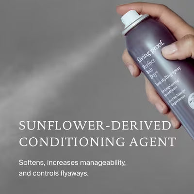 Hand spraying Living Proof PhD Heat Styling Spray; graphic highlights a sunflower-derived conditioning agent for softness and flyaway control
