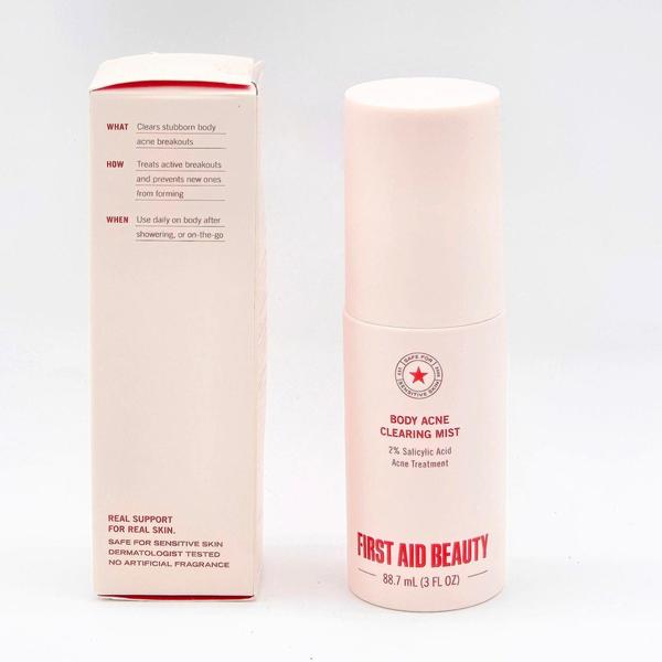 First Aid Beauty Body Acne Clearing Mist, a pale pink bottle with red text, next to its white and red box.