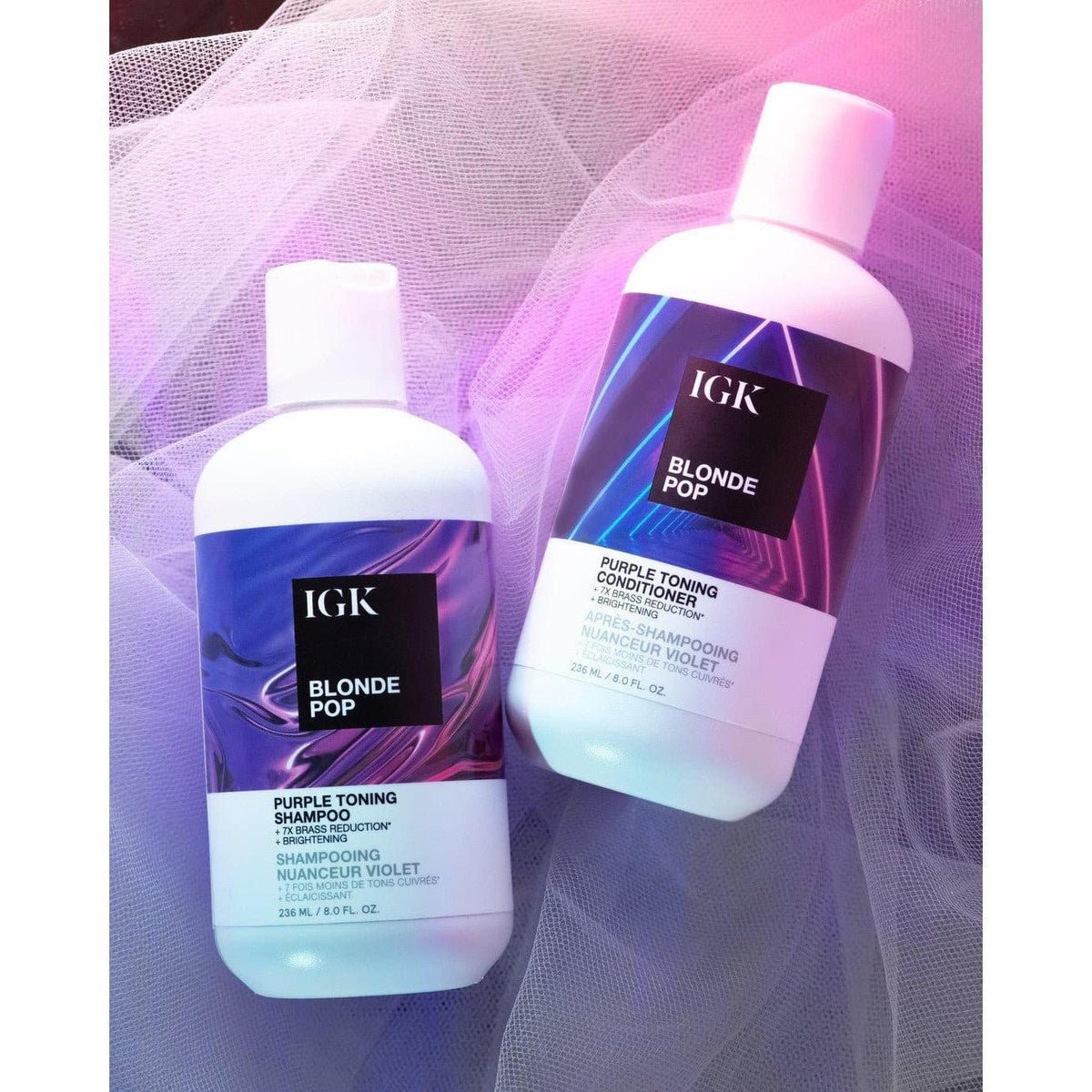 IGK Blonde Pop shampoo and conditioner, 8 fl oz / 236 mL each, resting on sheer fabric under pink and purple lighting.