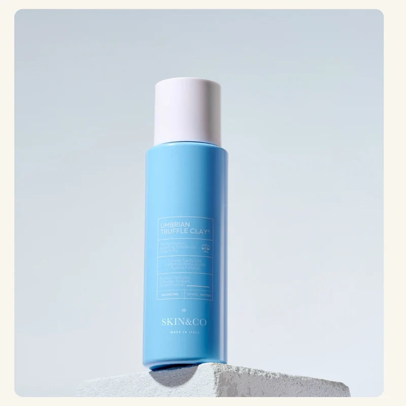 SKIN&CO Umbrian Truffle Clay Toning Potion blue bottle on a stone pedestal