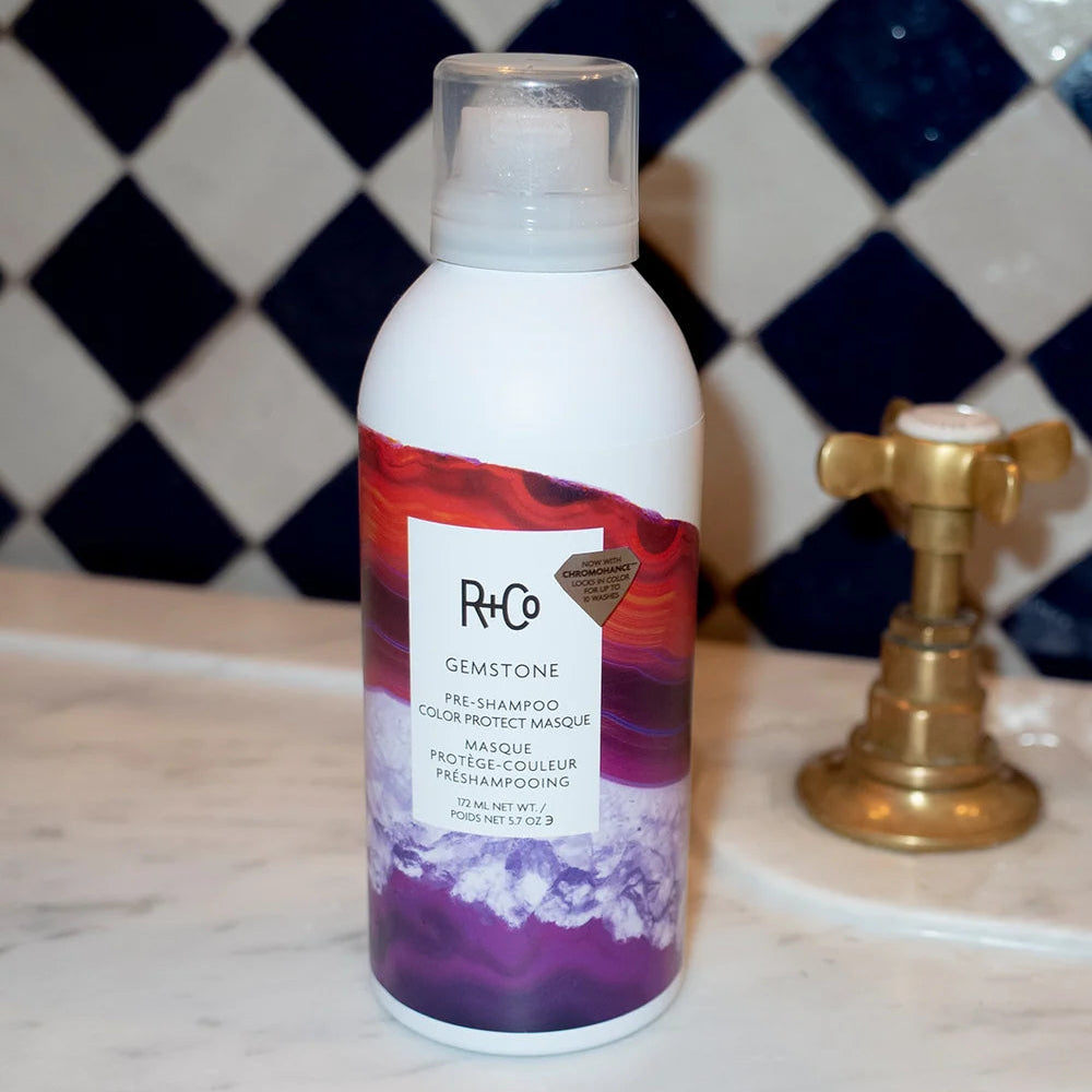 R+Co Gemstone masque can beside a brass tap on a bathroom counter with diamond-patterned tiles