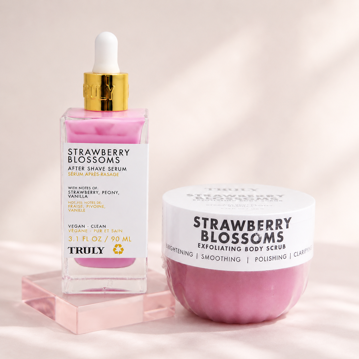 Truly Strawberry Blossoms serum and body scrub arranged on a soft pink editorial background