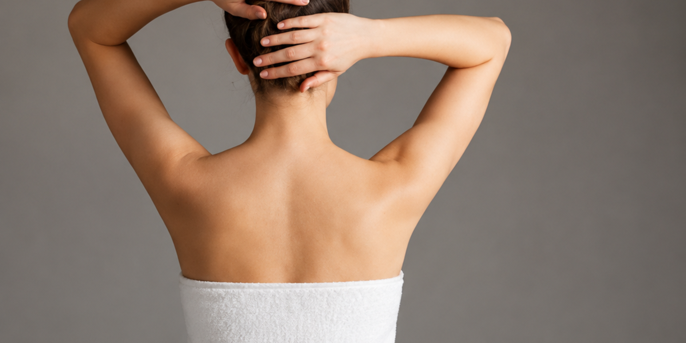 A woman wrapped in a white towel, photographed from behind for the Bare and Ready skin-care edit.
