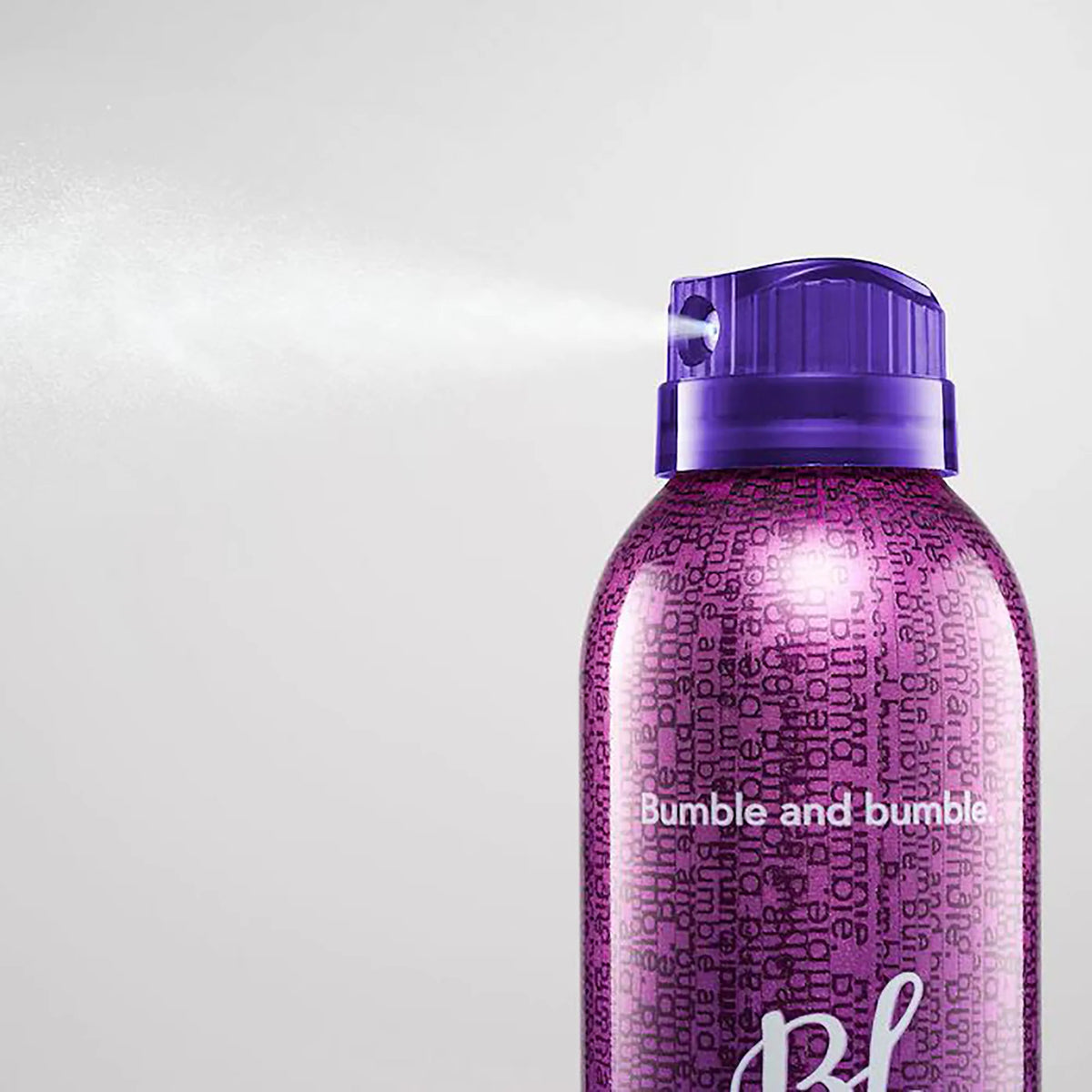 Close-up of the purple Bumble and bumble Spray de Mode aerosol can and twist-lock nozzle releasing a fine mist.
