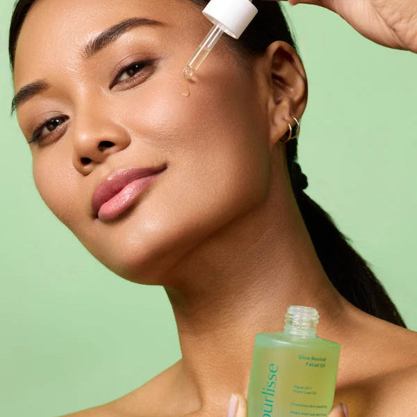 Model applying purlisse Glow Revival Facial Oil to her cheek with a dropper