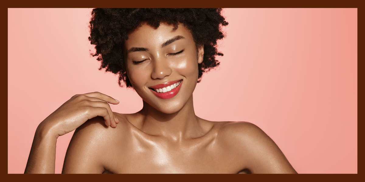 Smiling woman with natural curls and luminous skin against a warm peach background.