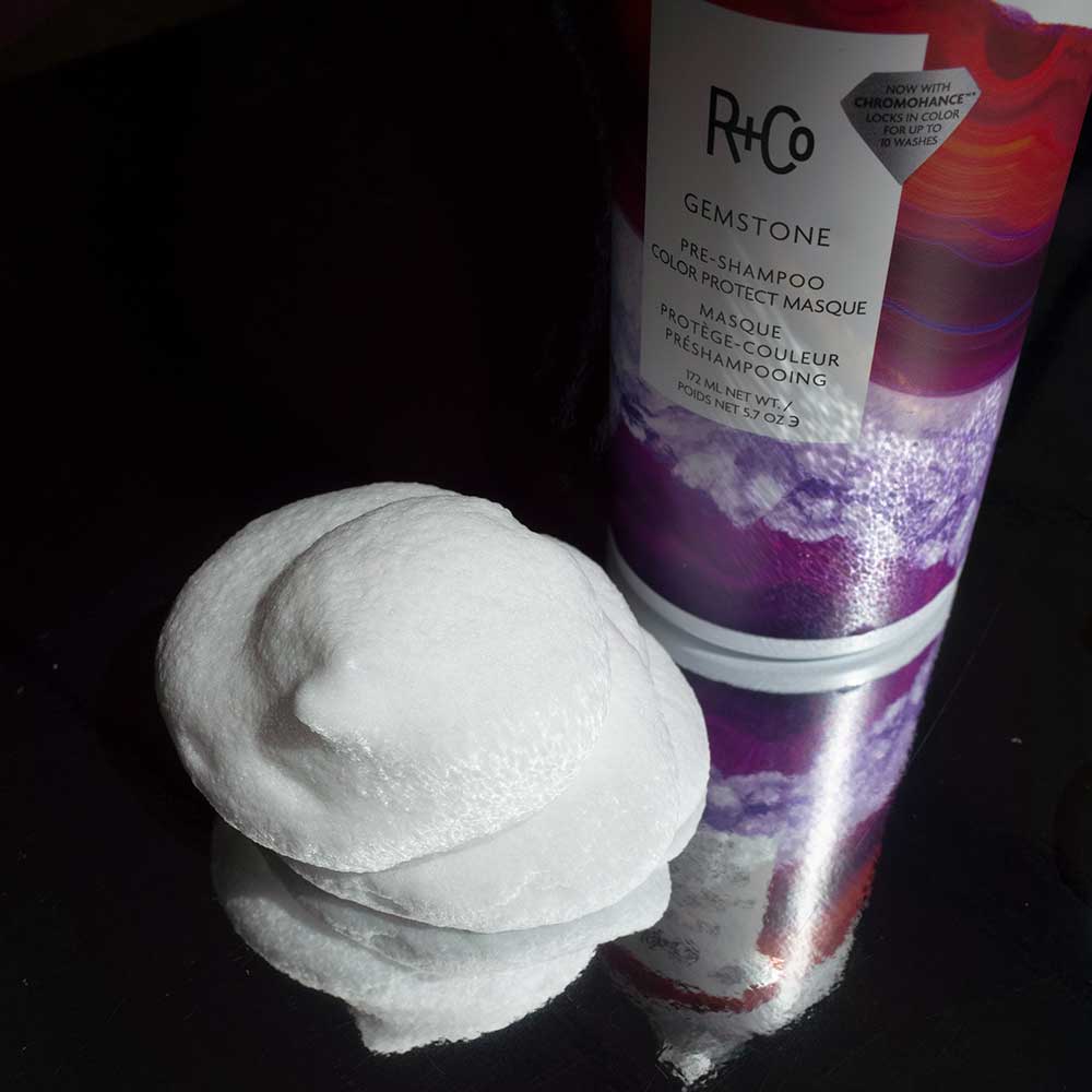 R+Co Gemstone Pre-Shampoo Color Protect Masque beside a dollop of white foam on a dark reflective surface