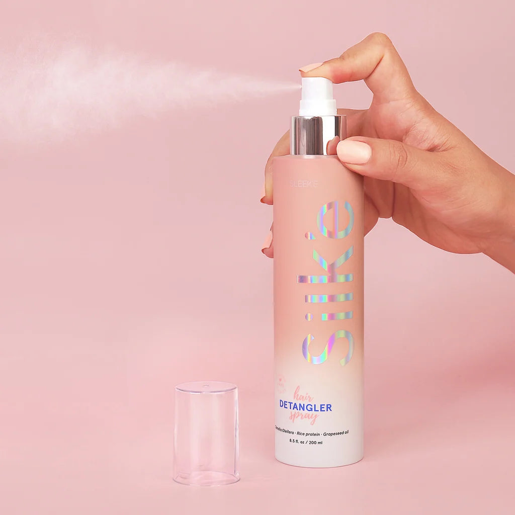 Hand spraying Sleek’e Silk’e Hair Detangler with the clear cap beside the bottle on pink