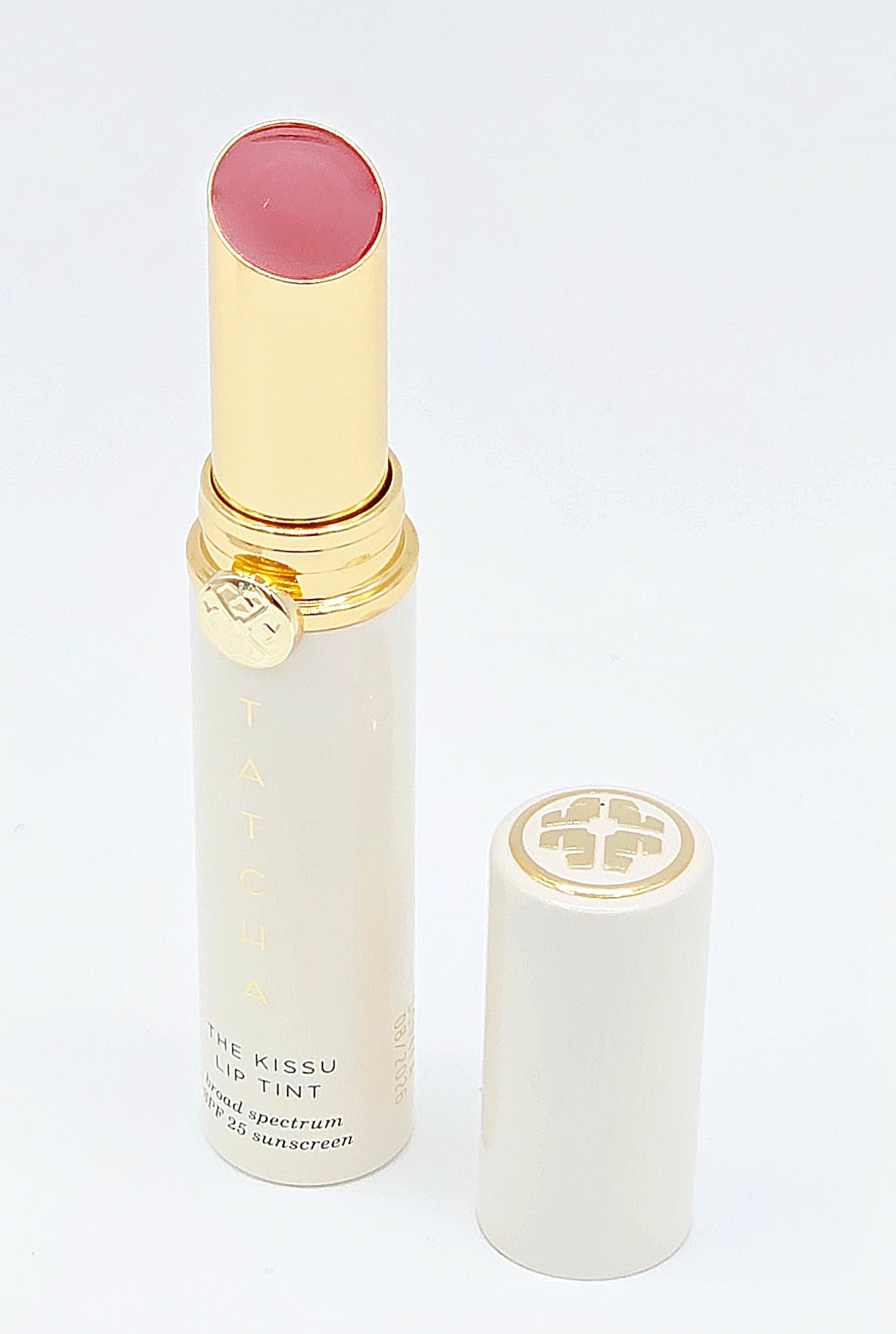 Lip tint with gold cap and white body on a light gray background