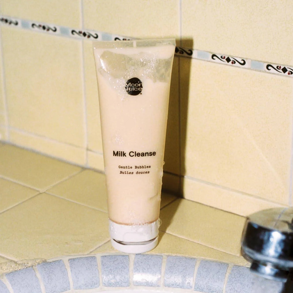 Milk Cleanse component tube with cleansing bubbles against yellow bathroom tiles