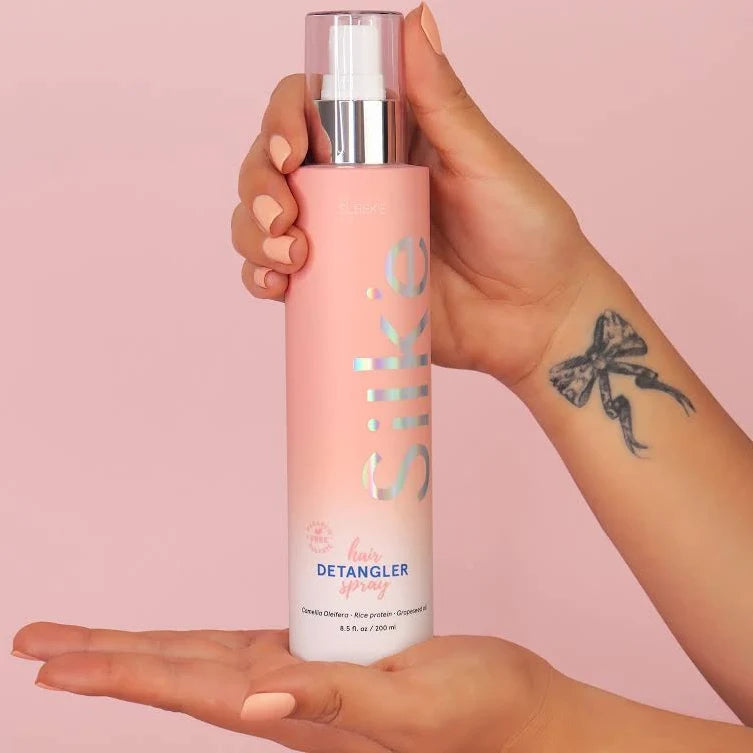 Hands holding Sleek’e Silk’e Hair Detangler Spray bottle against a pink background
