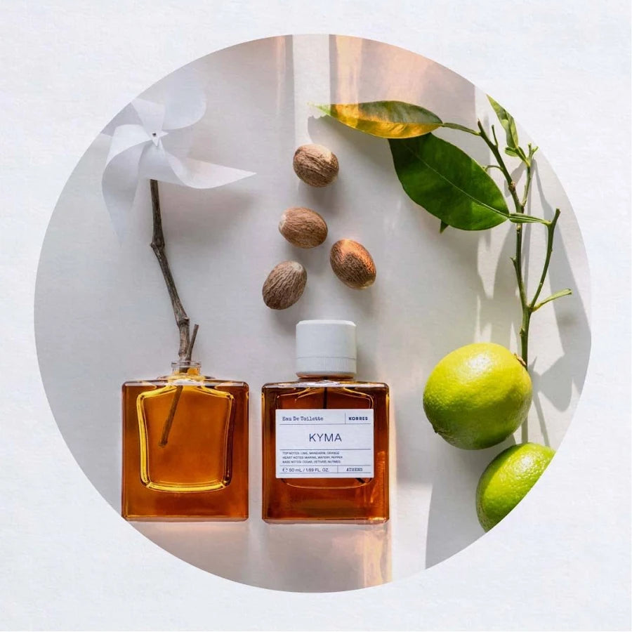 KORRES Kyma 50 mL bottle beside an amber glass bottle, limes, nutmeg and a white paper pinwheel
